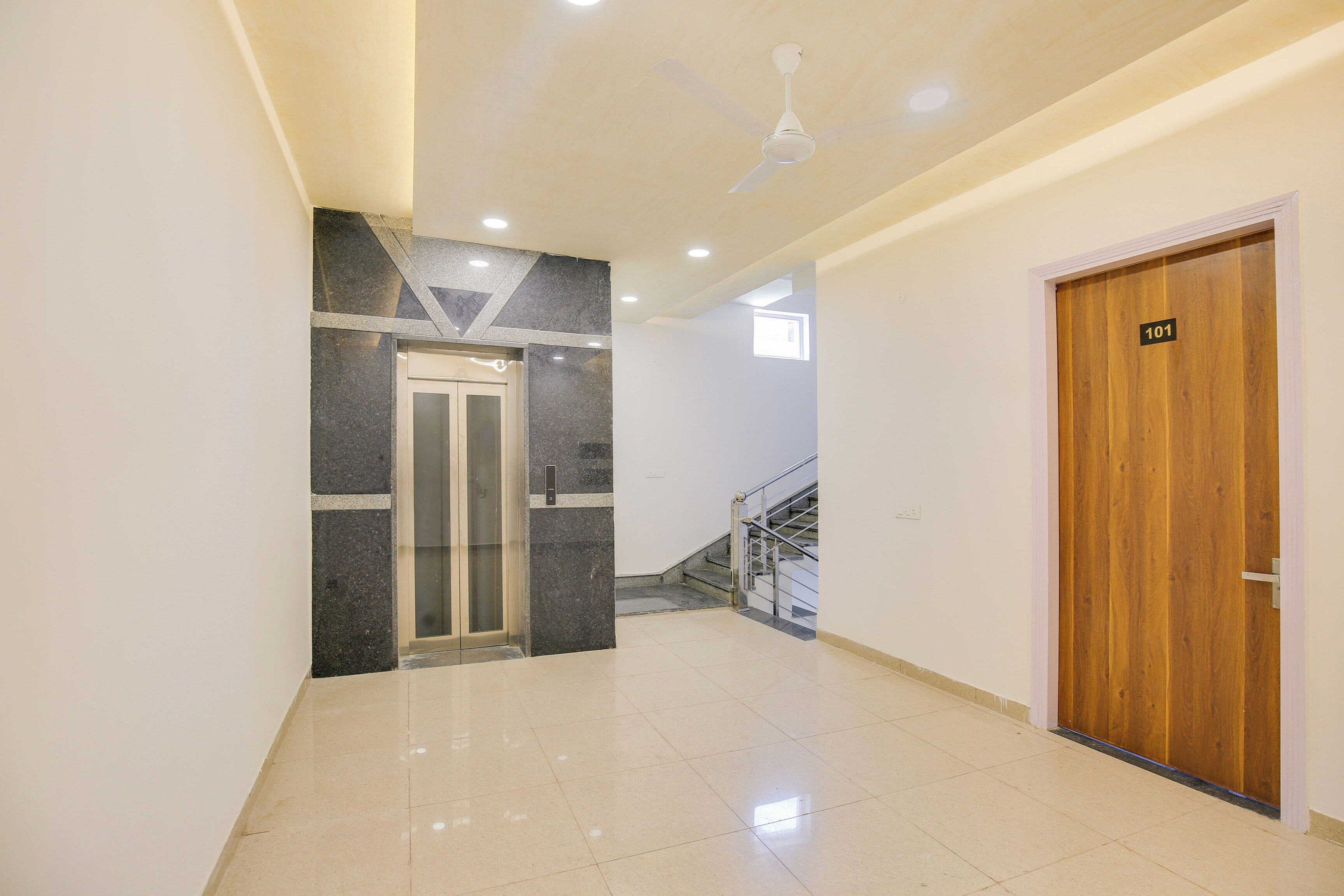A hallway with a wooden door labeled '101', a glass elevator, and a staircase with metal railings.