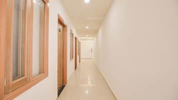 Un pasillo largo y estrecho con puertas y ventanas de madera en un lado, que conduce a una habitación luminosa con suelo de baldosas.