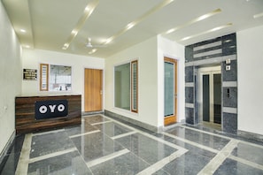 A hotel reception area with a reception desk, a wooden door, and a wall-mounted sign. - Hotel O by OYO GRAND STAY (Ludhiana)