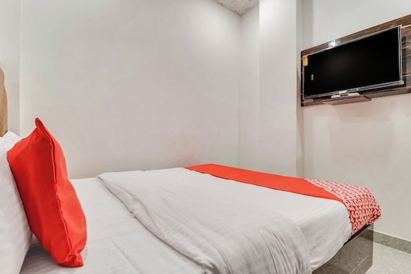 Quarto de hotel com cama, TV de tela plana na parede e manta com padrão vermelho e branco.