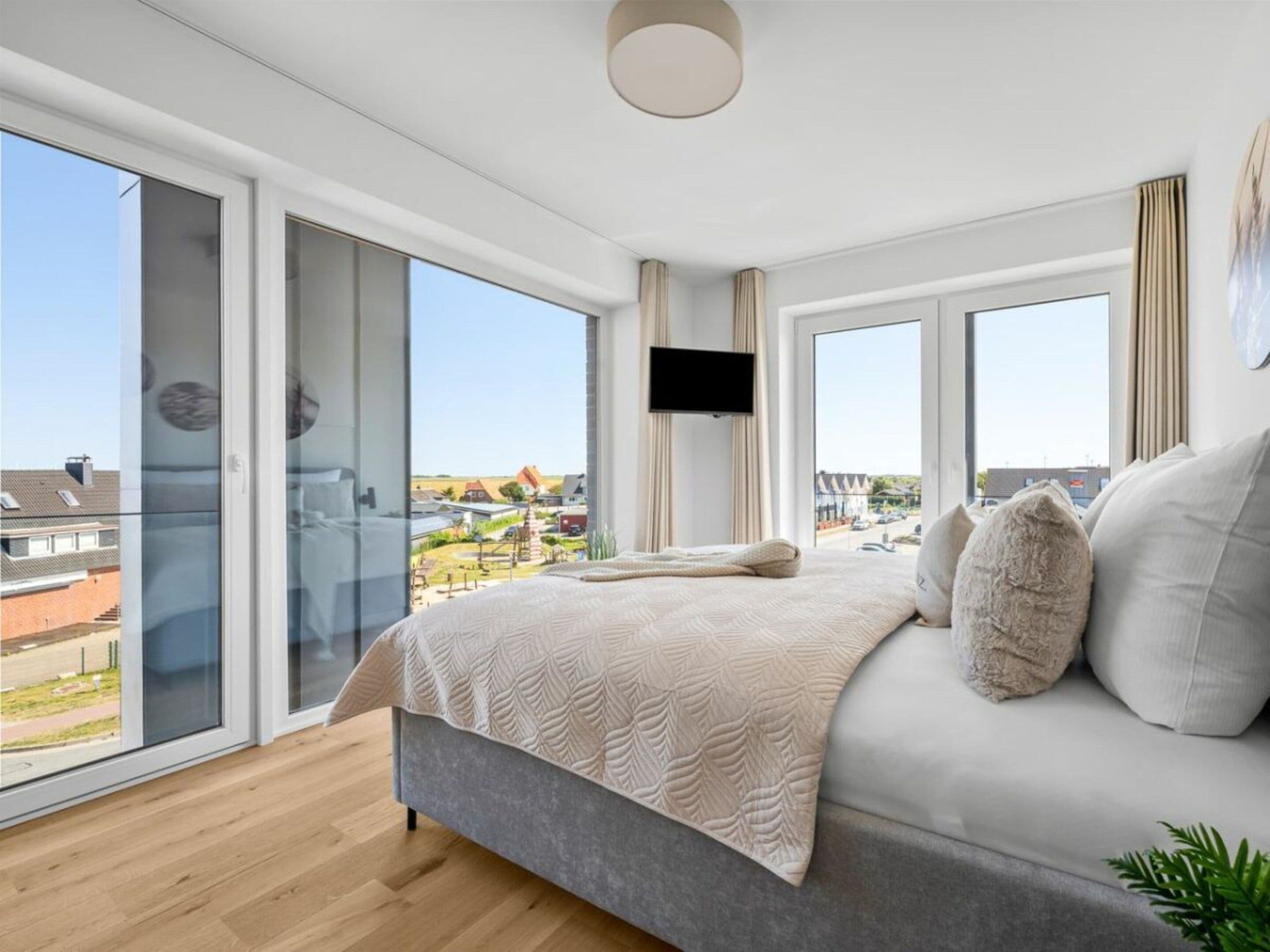 A modern bedroom with a large bed, a flat-screen TV, and a balcony with a city view.