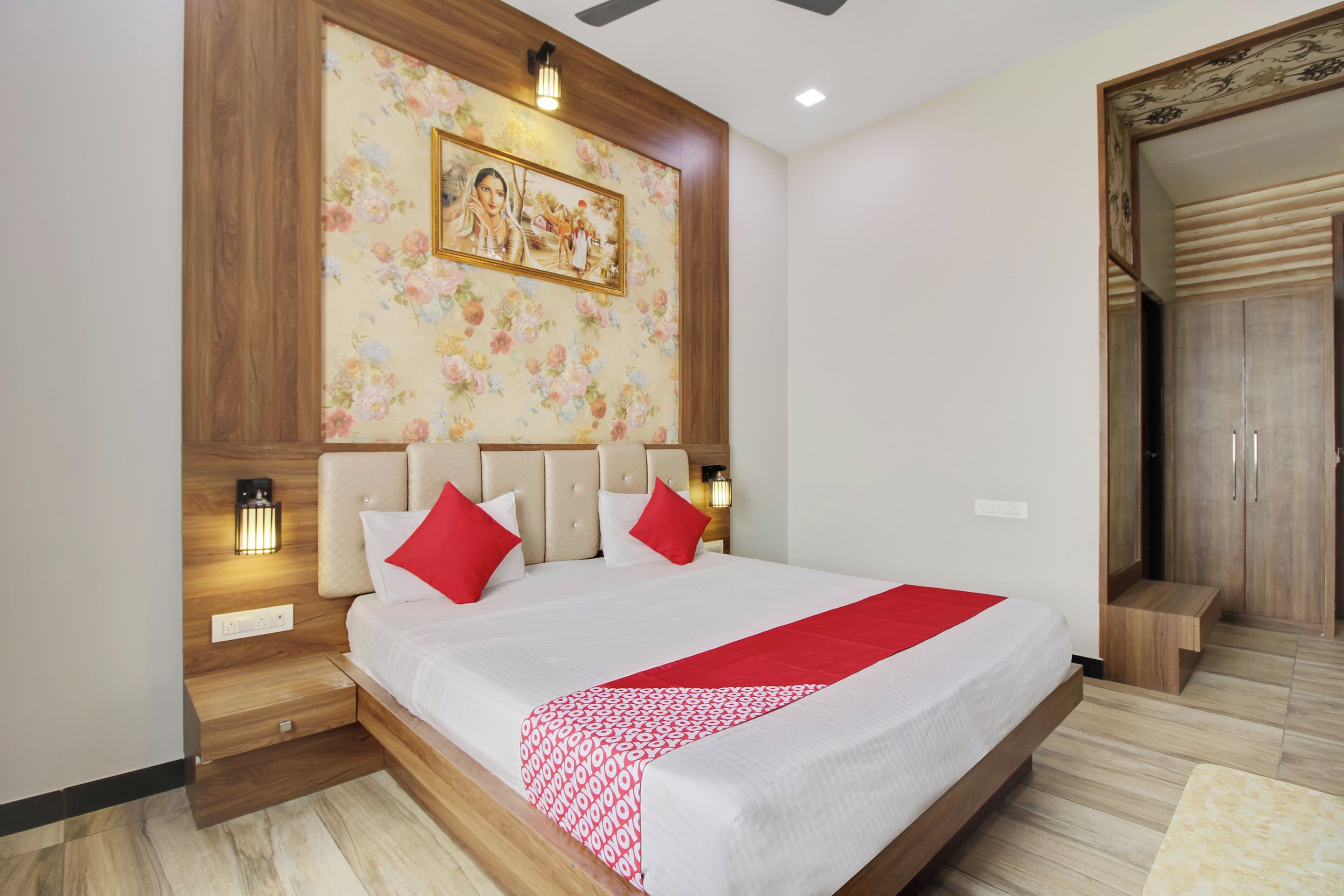 A bedroom with a large bed, wooden headboard, two bedside lamps, a floral wall decoration, and a wardrobe.