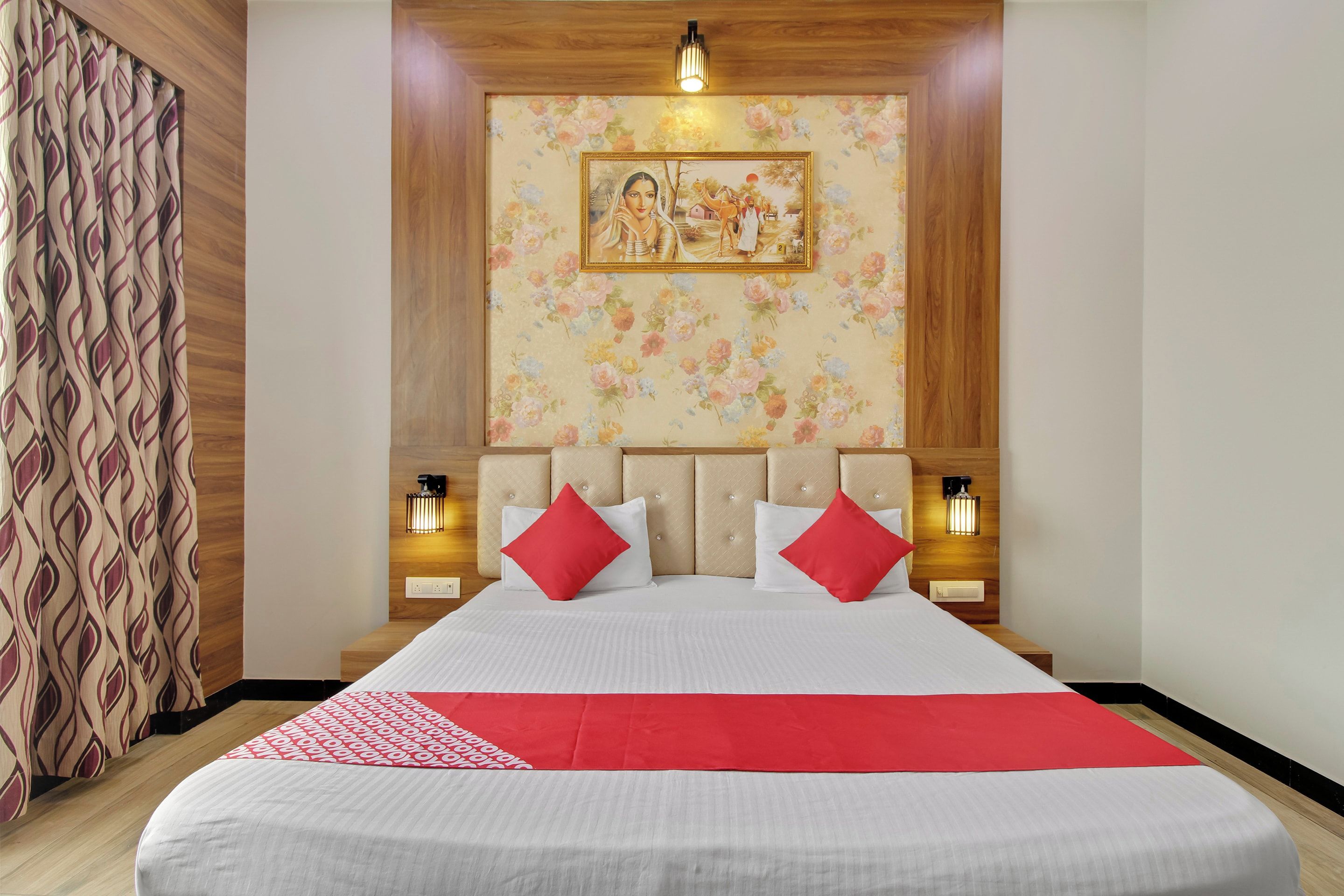 A hotel room with a large bed, floral wallpaper, a framed picture on the wall, and bedside lamps.