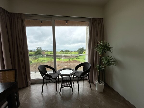 Ein Zimmer mit einer großen Schiebeglastür, die auf eine grüne Landschaft hinausführt. Im Inneren befindet sich ein runder Tisch mit zwei Stühlen und einer Topfpflanze.