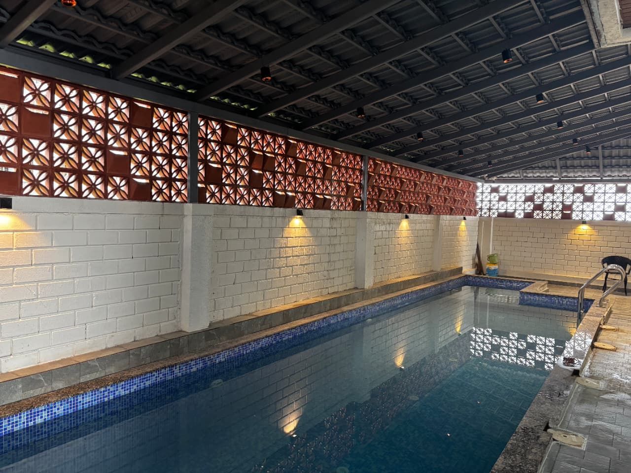 Ein Innenpool mit gefliestem Boden und Wänden, einer Backsteinwand auf der einen Seite sowie einem dekorativen Trennwerk mit geometrischen Mustern.
