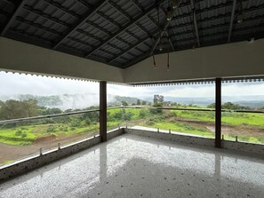 A spacious room with a high ceiling, large windows, and a view of a green landscape.