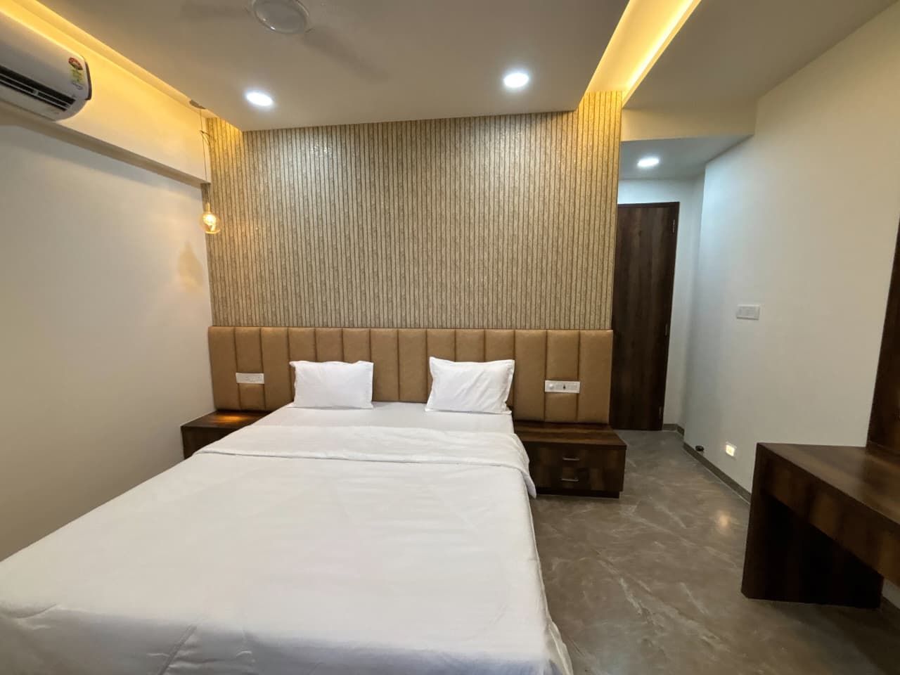 Ein Hotelzimmer mit einem großen Bett, einem Holzkopfbrett, Nachttischen und einer Wand-Klimaanlage.