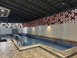 Una piscina interior con suelo de baldosas, barandilla metálica y pared de ladrillo con diseño decorativo.