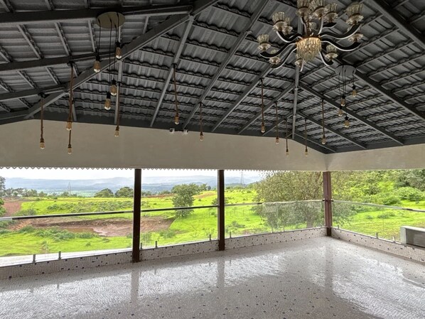 A spacious room with a high ceiling, large windows, and a view of a green landscape.