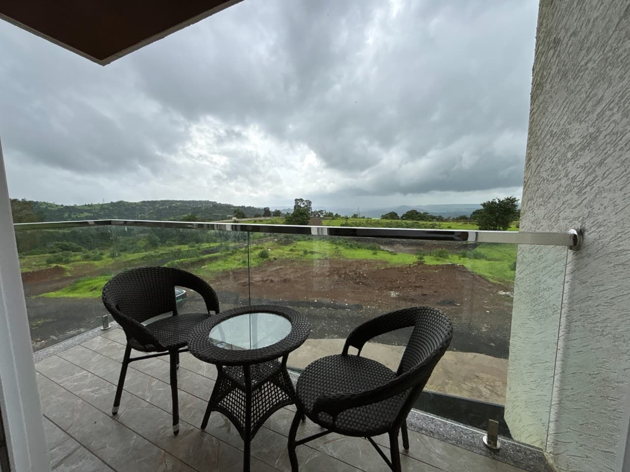 A balcony with a glass railing, two wicker chairs, and a small round table.