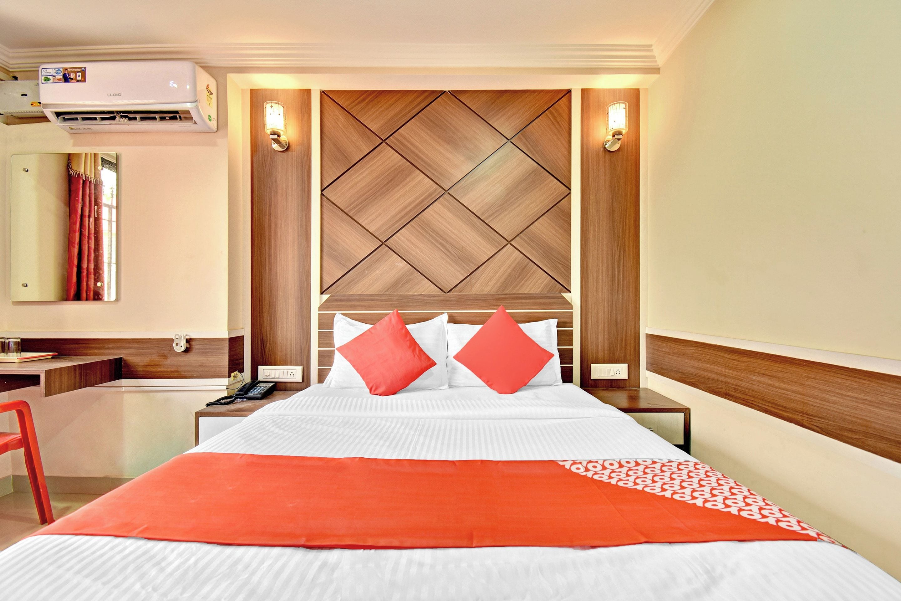 Habitación de hotel con cama, escritorio, silla, aire acondicionado y lámpara de pared.