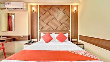 Habitación de hotel con cama, escritorio, silla, aire acondicionado y lámpara de pared.