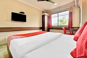 Una habitación de hotel con una cama, un televisor montado en la pared, una ventana con cortinas y una silla roja.