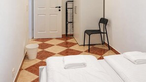 A hotel room with two beds, a chair, a trash bin, and a door leading to a bathroom. - One More Night in Vienna 1BR and Living Room (Vienna)