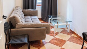 A living room with a sofa, a glass coffee table, a chair, and a tiled floor. - One More Night in Vienna 1BR and Living Room (Vienna)
