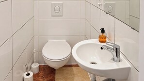 A bathroom with a toilet, sink, and a hand soap dispenser. - One More Night in Vienna 1BR and Living Room (Vienna)