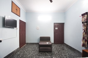 Ein Zimmer mit einem an der Wand befestigten Fernseher, einer Couch, zwei Türen und einem Deckenventilator.