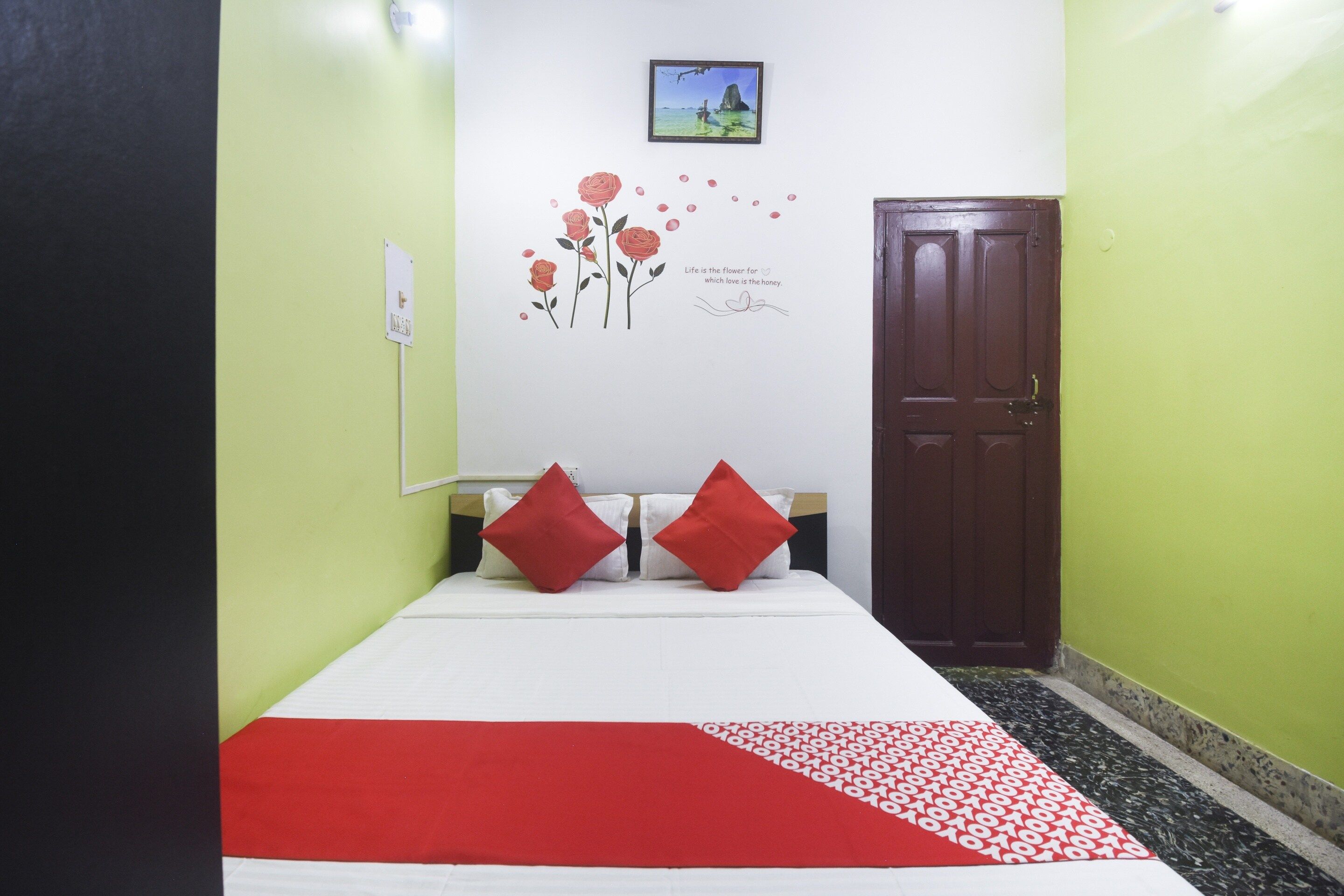 Una habitación con una cama, una puerta y una pared decorada con un adhesivo floral y una pequeña fotografía.