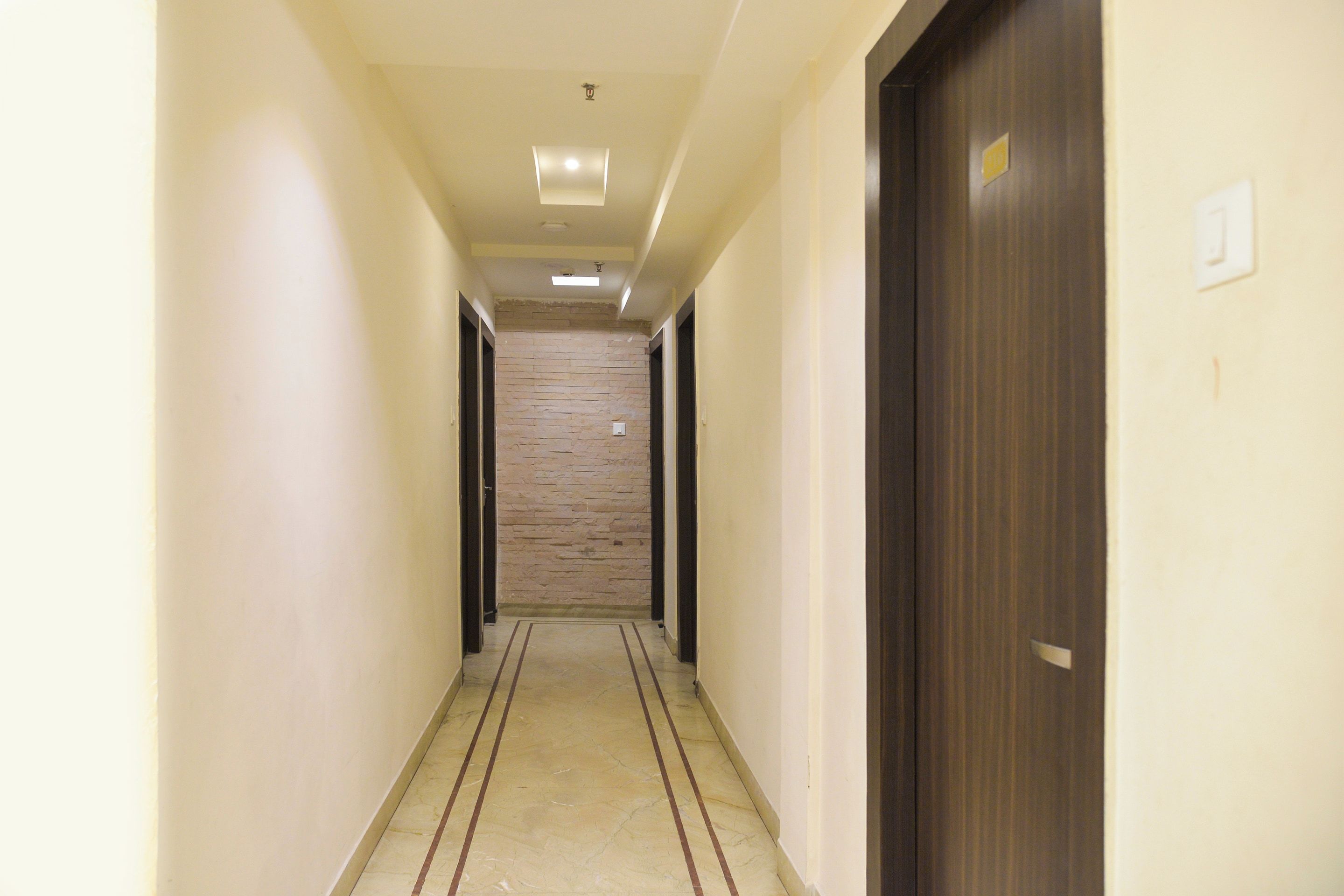 A hotel hallway with a stone wall, wooden doors, and a tiled floor.