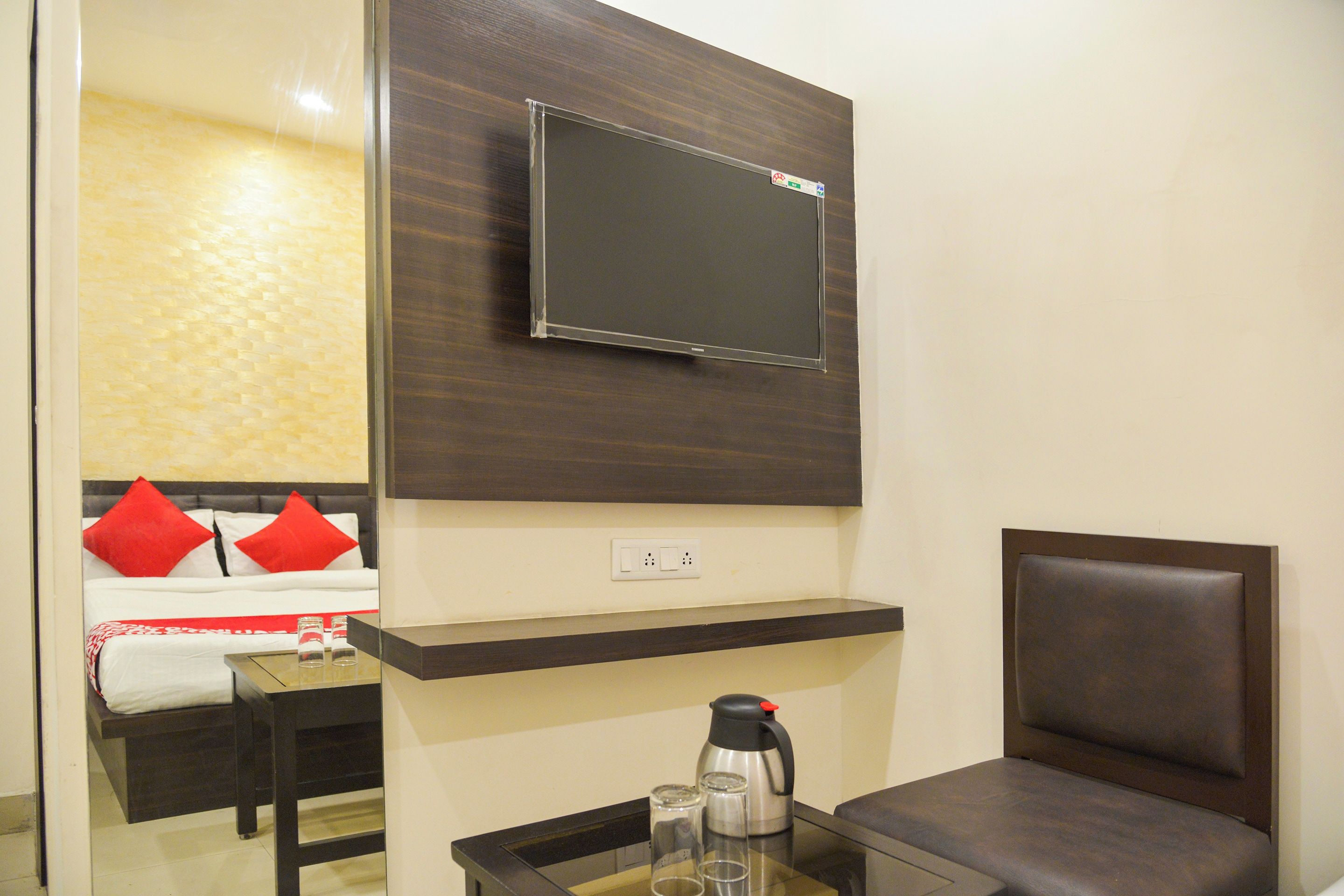 A modern living room with a mounted flat-screen TV, a sofa with red cushions, a coffee table with a kettle and glasses, and a wall-mounted shelf.