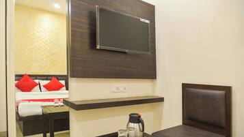 A modern living room with a mounted flat-screen TV, a sofa with red cushions, a coffee table with a kettle and glasses, and a wall-mounted shelf.