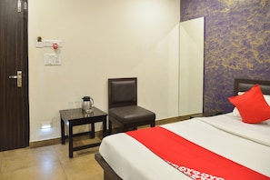A hotel room with a bed, a chair, a small table with a coffee pot, and a mirror. - Collection O De Sivalika Boutique Near (Kolkata)