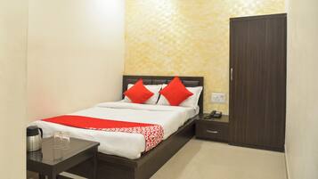 A hotel room with a bed, a nightstand, a table with a thermos and glasses, and a wardrobe.
