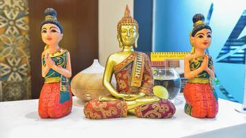 Three statues of a seated figure in traditional attire, a white vase, and a blue patterned wall.