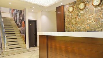 A hotel reception area with a staircase, a wall with clocks, and a door marked with the number 102.