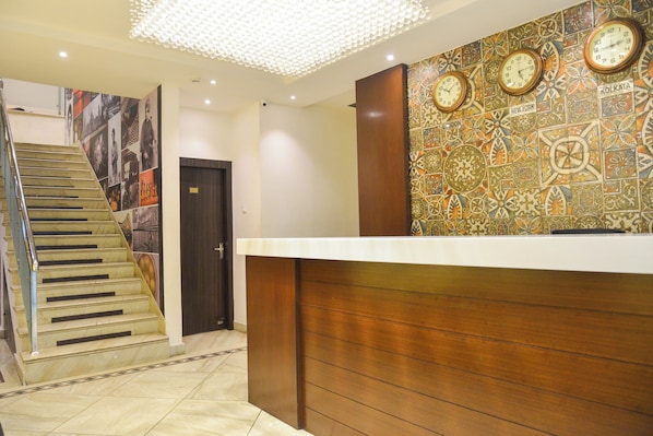 A hotel reception area with a staircase, a wall with clocks, and a door marked with the number 102.