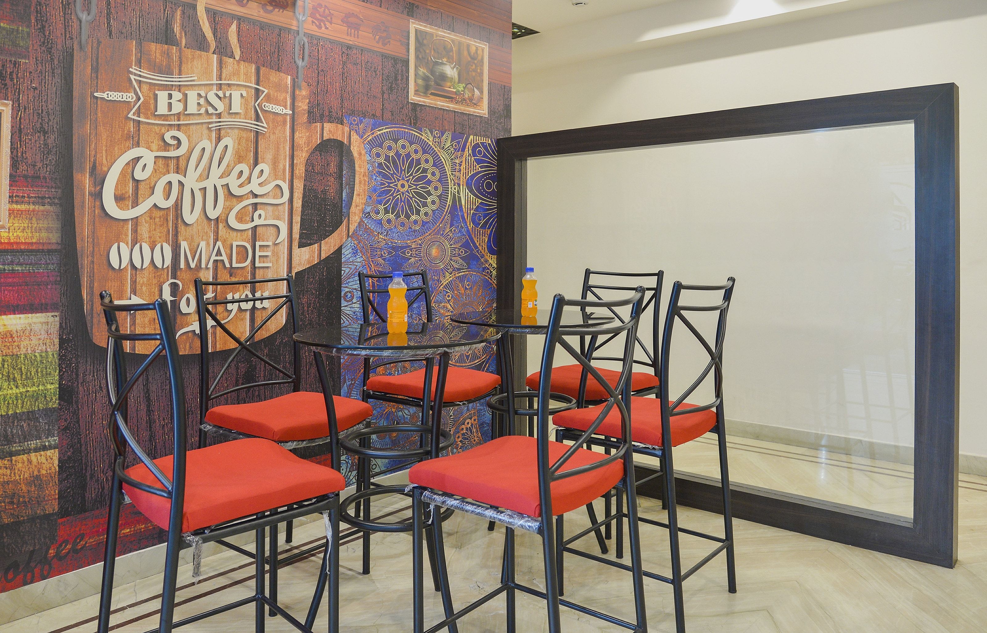 A meeting room with a coffee-themed wall, a glass table, and four chairs with red cushions.