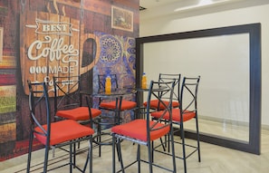 A meeting room with a coffee-themed wall, a glass table, and four chairs with red cushions. - Collection O De Sivalika Boutique Near (Kolkata)