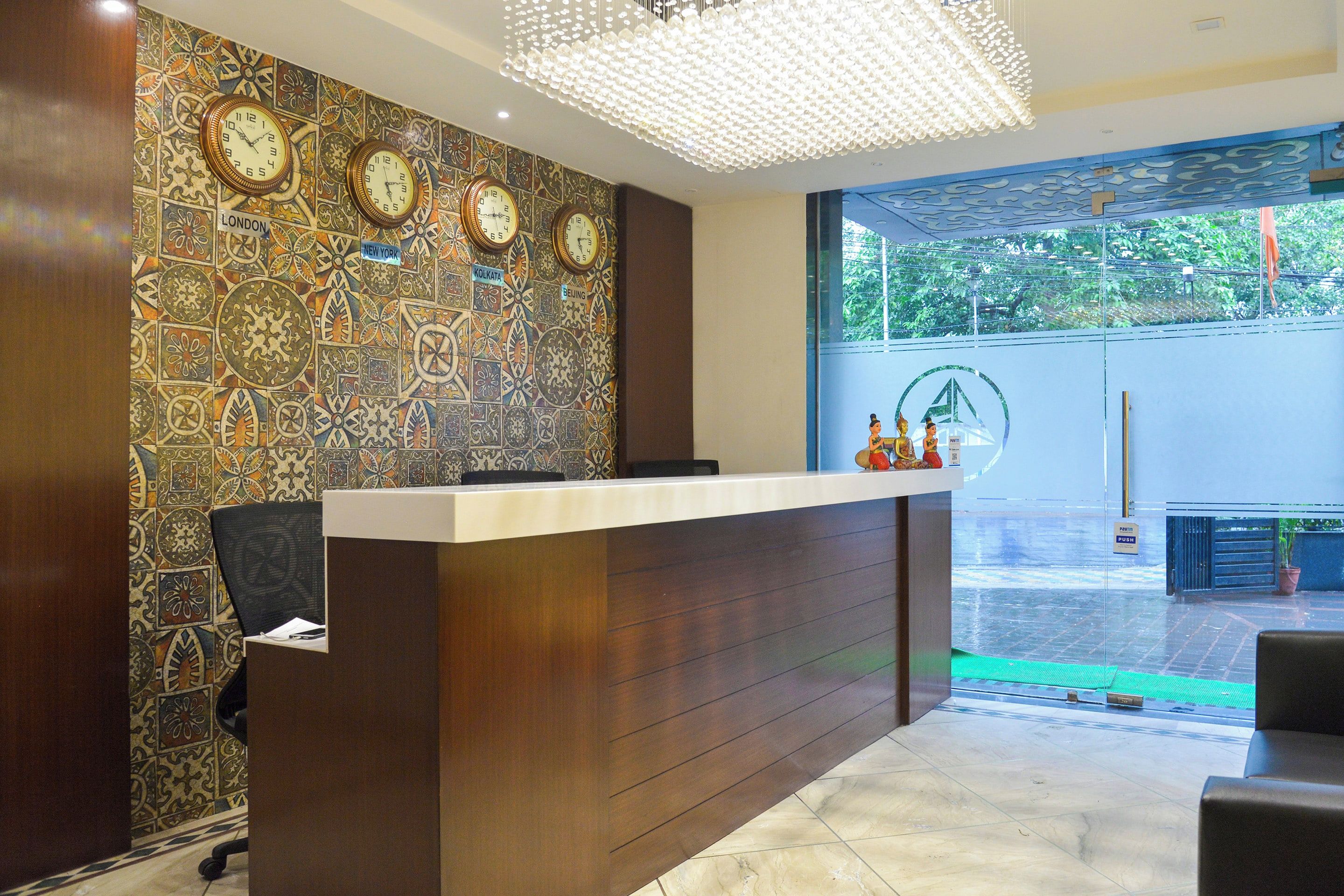 A reception desk with a clock wall, a chandelier, and a view of a green outdoor area.