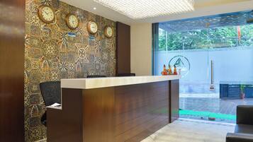 A reception desk with a clock wall, a chandelier, and a view of a green outdoor area.