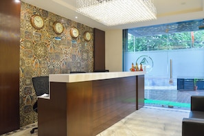 A reception desk with a clock wall, a chandelier, and a view of a green outdoor area. - Collection O De Sivalika Boutique Near (Kolkata)