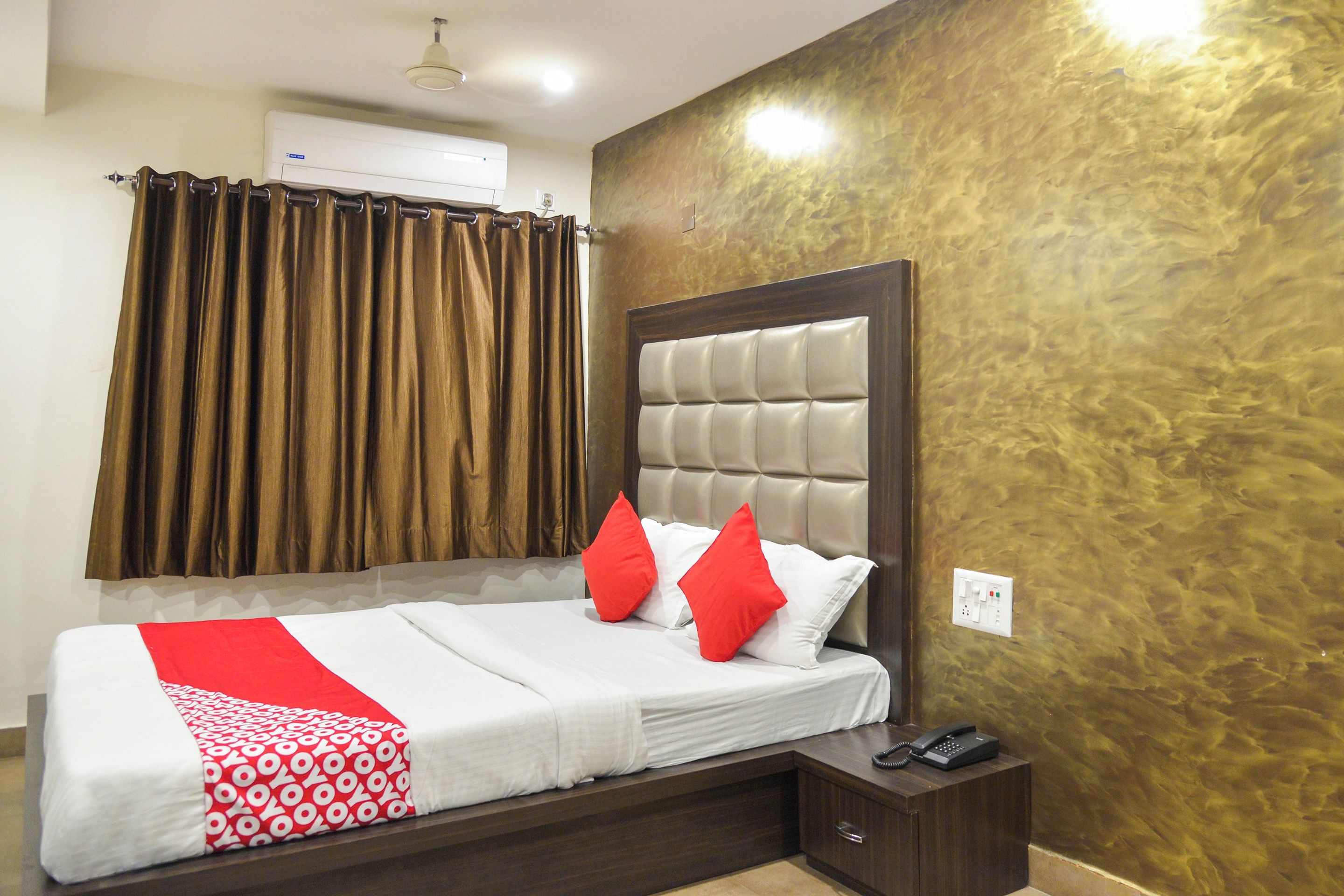 A hotel room with a bed, a bedside table with a phone, and a wall-mounted air conditioner.