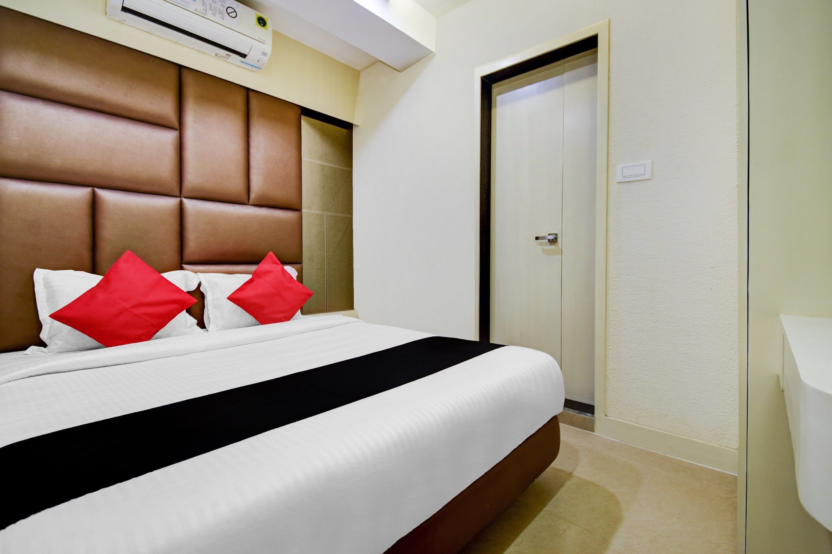 Una habitación de hotel con una cama grande, cabecera, una puerta y un equipo de aire acondicionado.