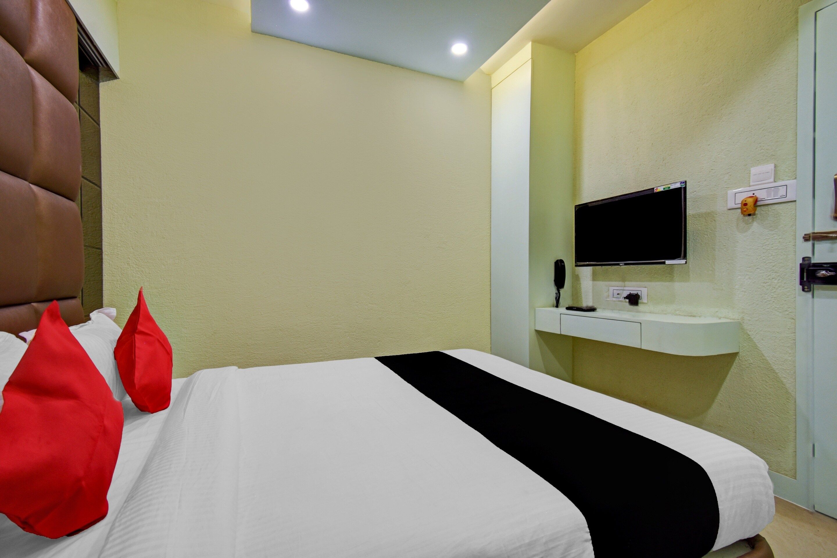 Une chambre d’hôtel avec un lit, un téléviseur fixé au mur et un petit bureau avec un téléphone.