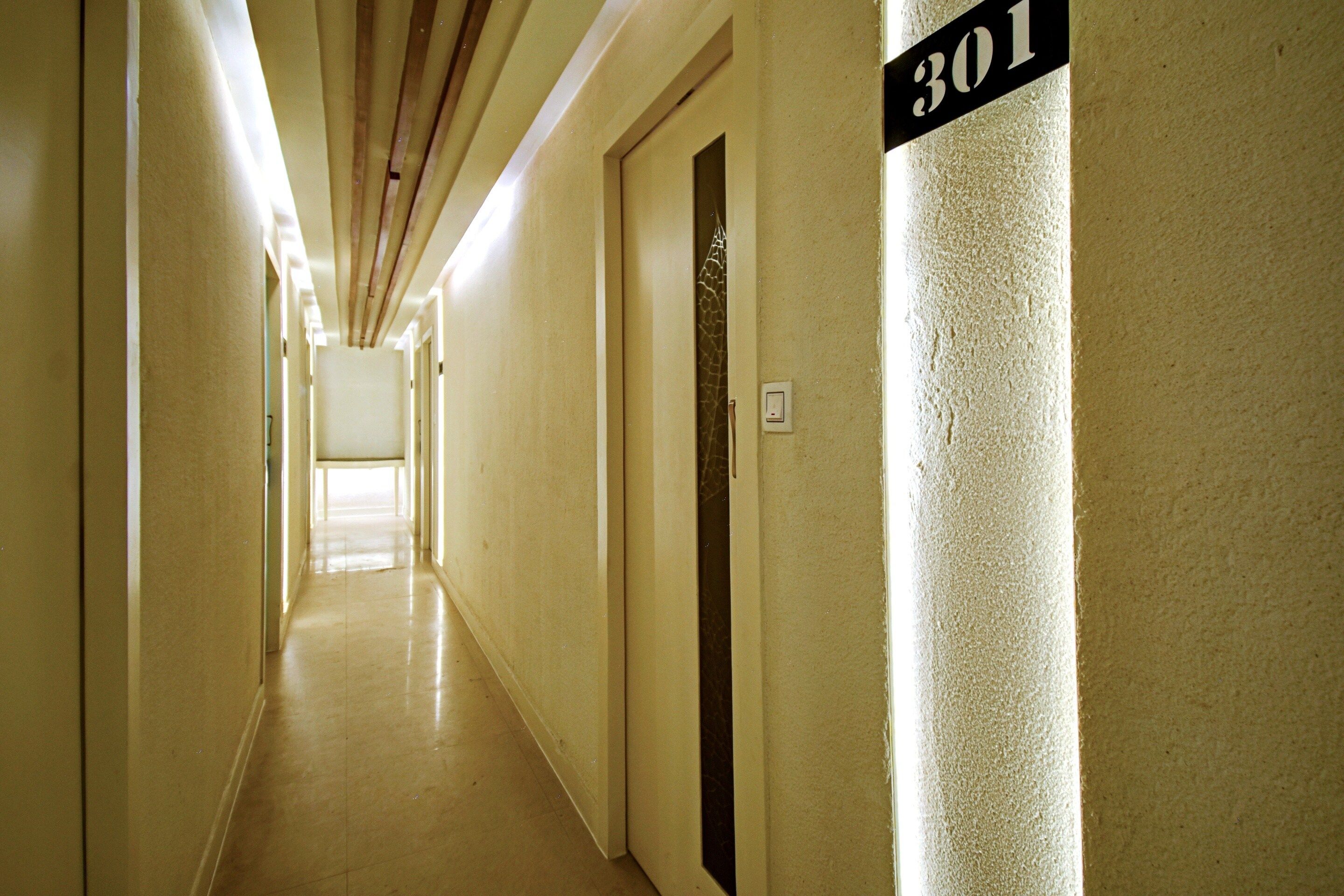 A hotel corridor with a number sign indicating room 301, a door with a giraffe pattern, and a light switch on the wall.
