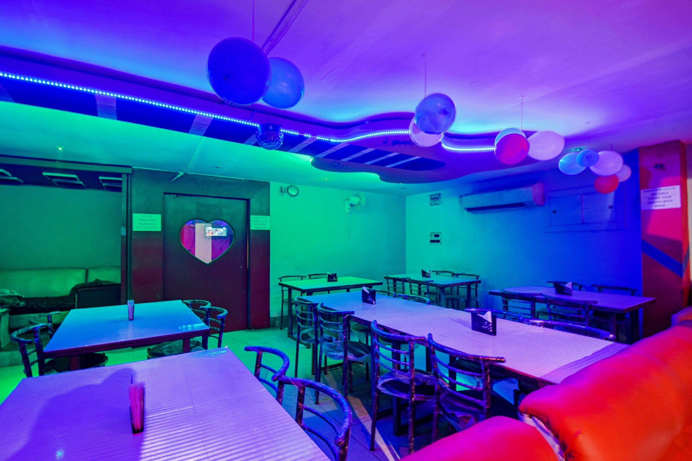 Una habitación con mesas y sillas, una decoración con forma de corazón en la pared y un cartel con instrucciones de higiene.