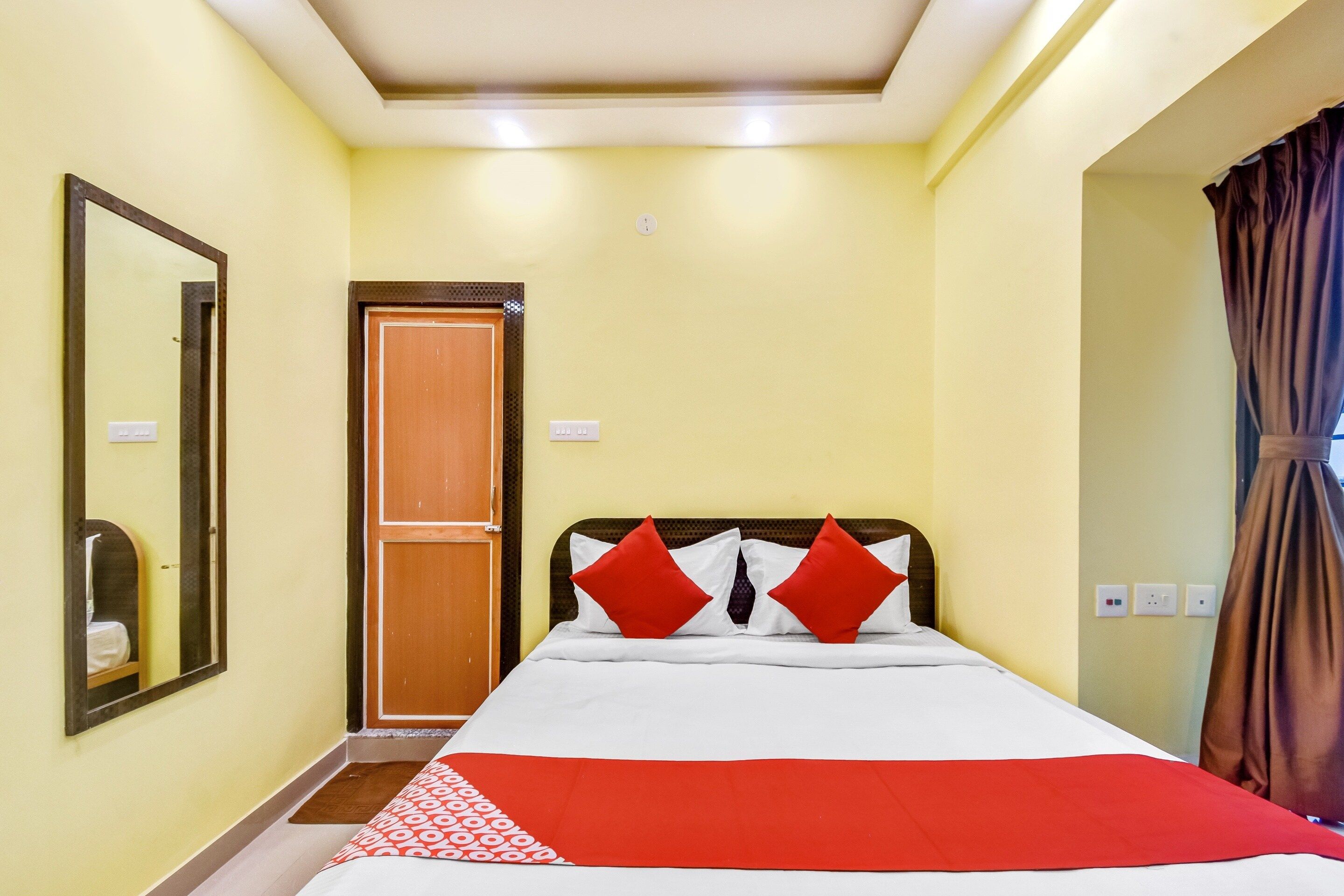 A hotel room with a bed, a mirror, a door, and a curtain.