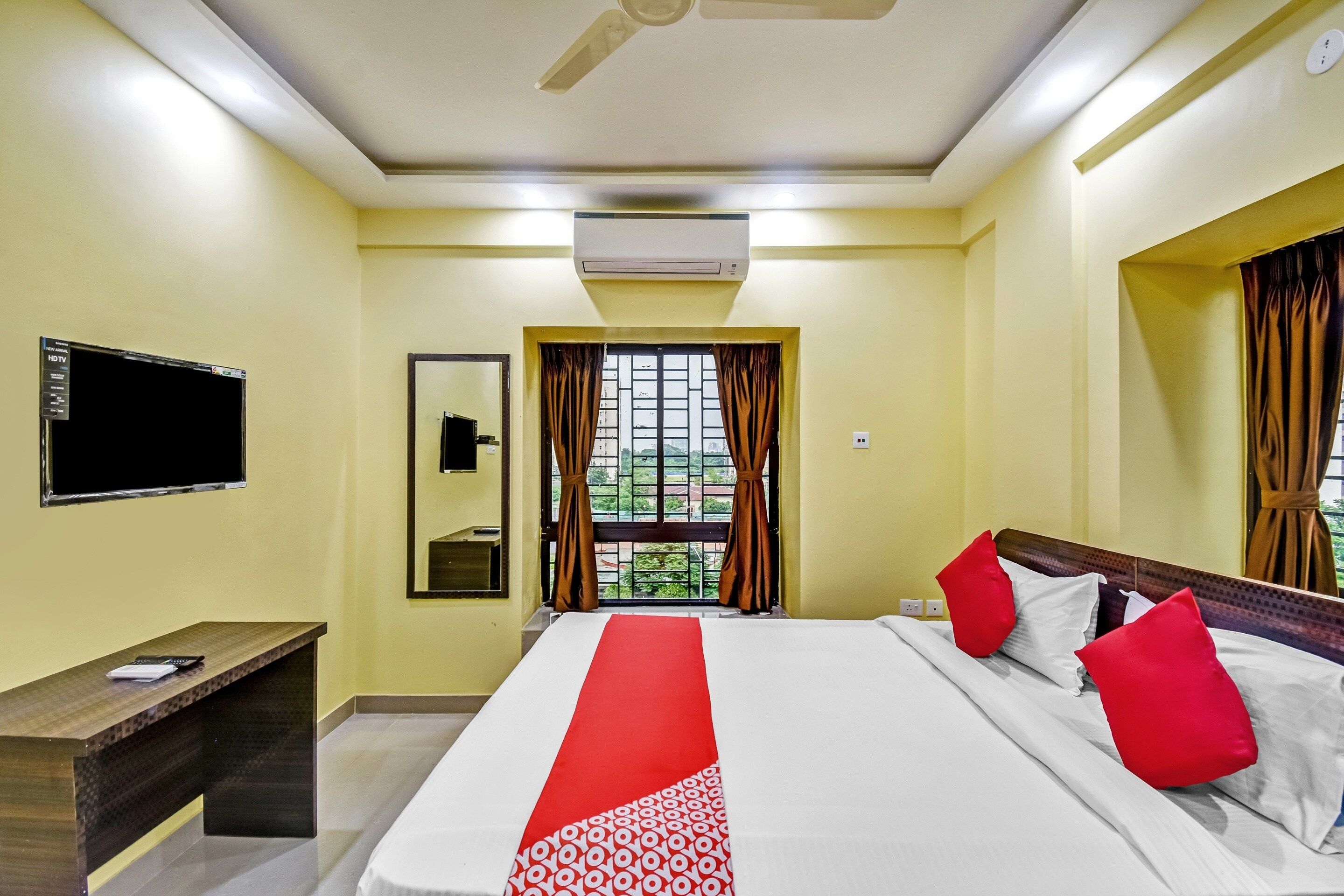 A hotel room with a bed, a desk, a flat-screen TV, and a window with curtains.