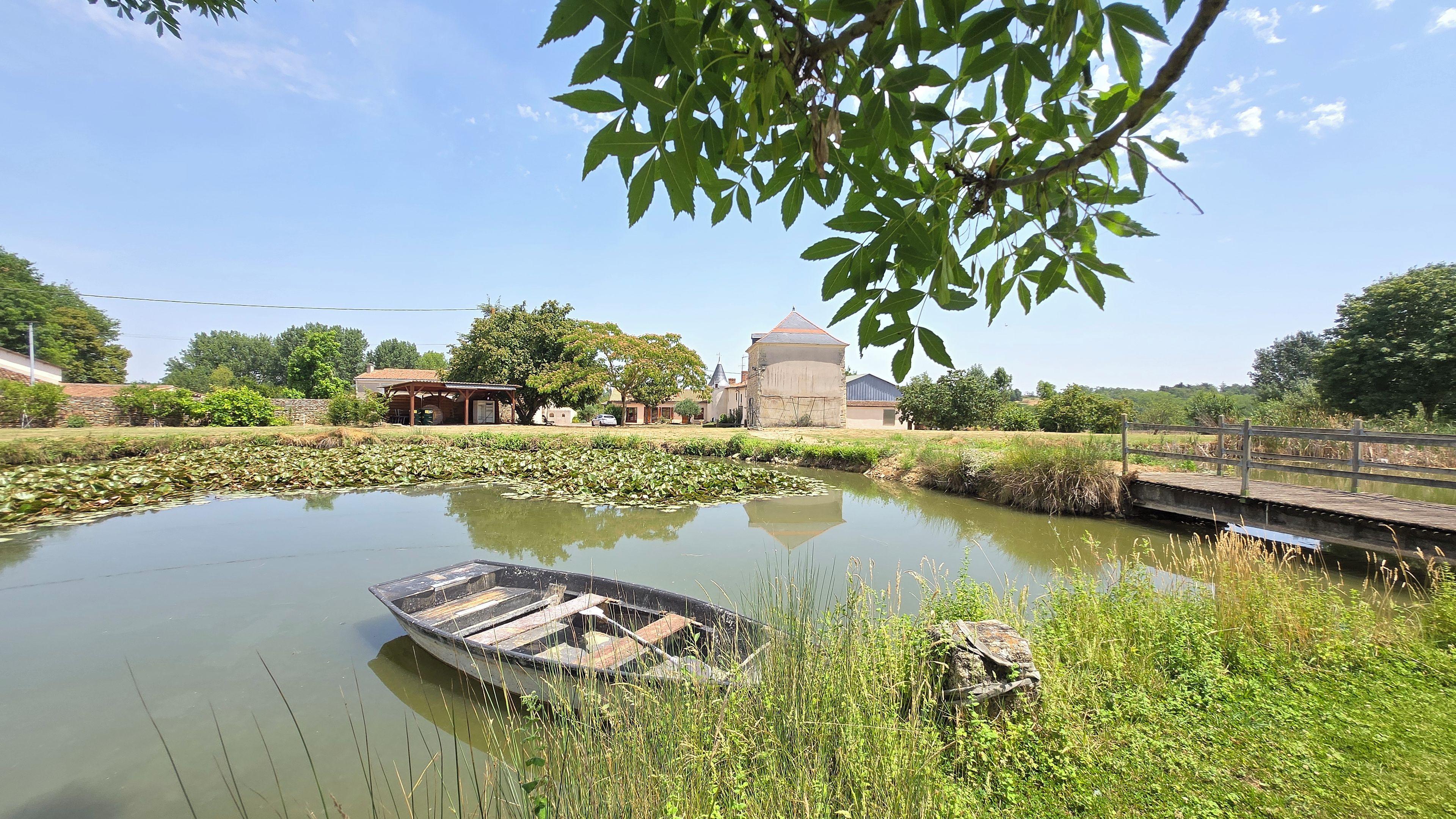 A tranquil pond with a small boat, surrounded by lush greenery and a traditional building in the background.