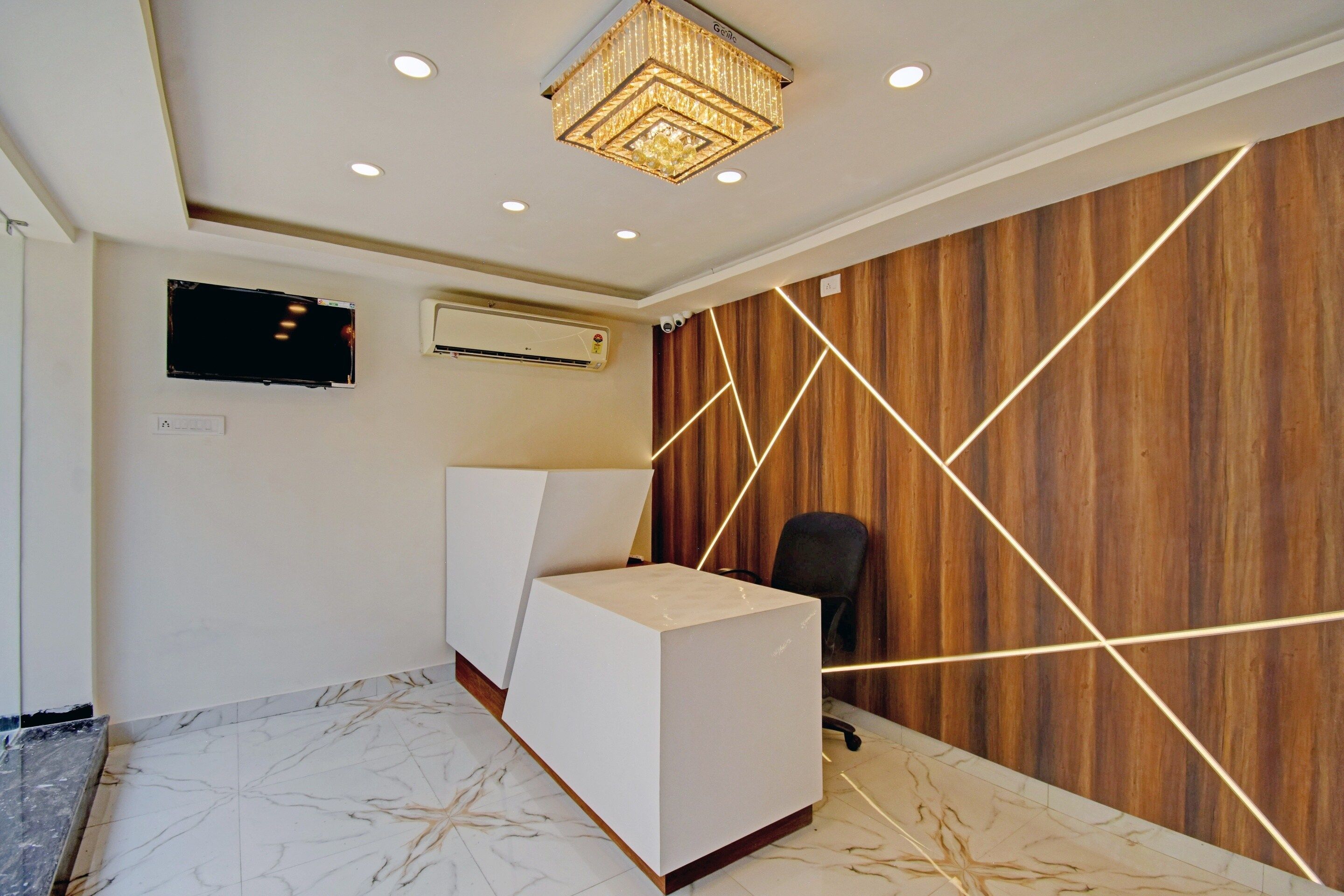 Een receptie met een wit aanrecht, een wandgemonteerde flatscreen-tv, een airconditioning en een houten wand met geometrische verlichting.