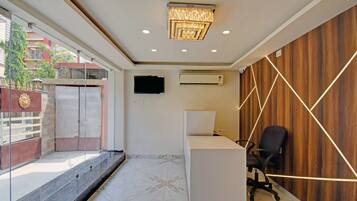 An office interior with a reception desk, a mounted flat-screen TV, an air conditioning unit, and a wooden wall with geometric lighting.