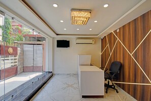 Un interior de oficina con un mostrador de recepción, un televisor de pantalla plana montado en la pared, una unidad de aire acondicionado y una pared de madera con iluminación geométrica.