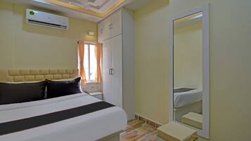 A hotel room with a bed, a wardrobe, a mirror, and an air conditioning unit.