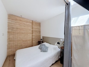 Quarto com cama, mesa de cabeceira, luminária e janela com cortinas.