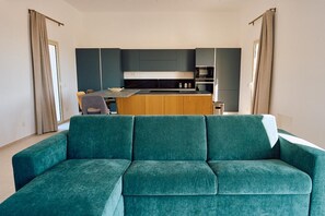 Een moderne woonkamer met een blauwgroene bank, een keuken op de achtergrond en een eethoek.
