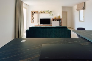 A modern living room with a flat-screen TV, a green sofa, and a dining area with a table and chairs. - New Listing (Sicilia)